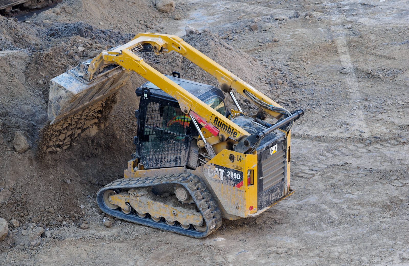Cat 299D compact track loader dumping dirt on a job site